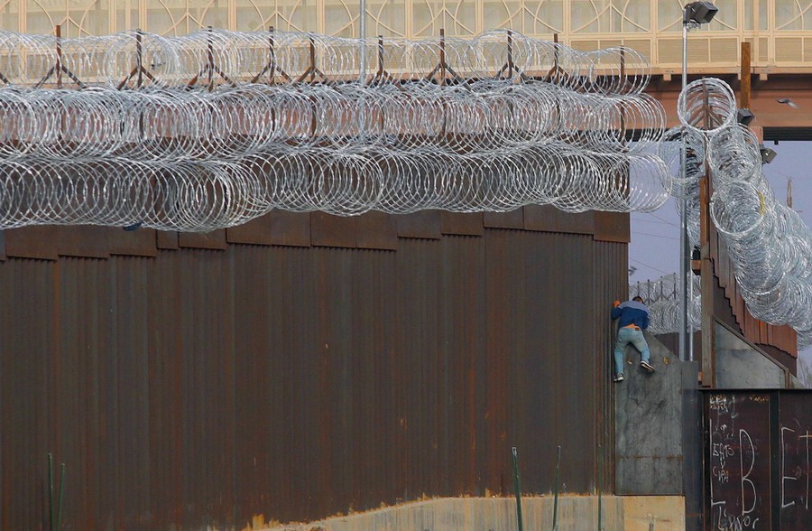 A person scales part of a large border fence.