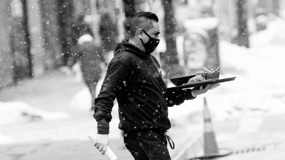 A restaurant server holds a tray while walking outside in the snow.