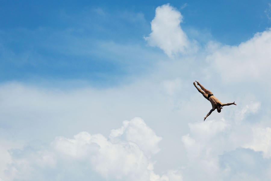 A high diver falls through the air, with only clouds and blue sky visible behind them.