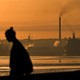 The silhouette of a person in front of a backdrop of an oil refinery in Havana, with an orange, smoky sky