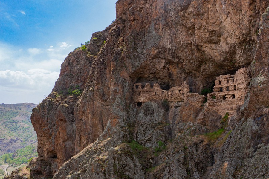 Ruins of a mountain monastery sit inside a cave in a cliff wall.