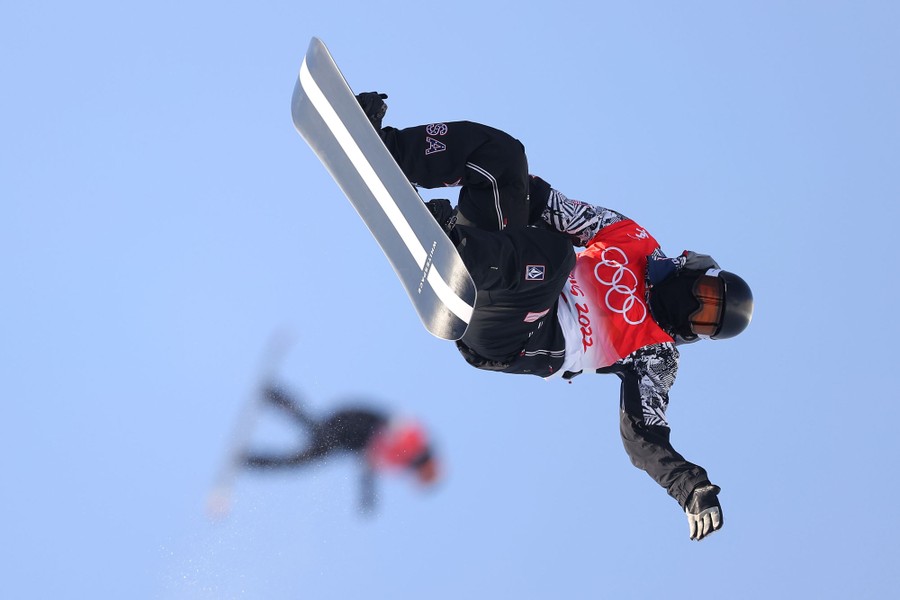 Two snowboarders are seen practicing before a halfpipe event.