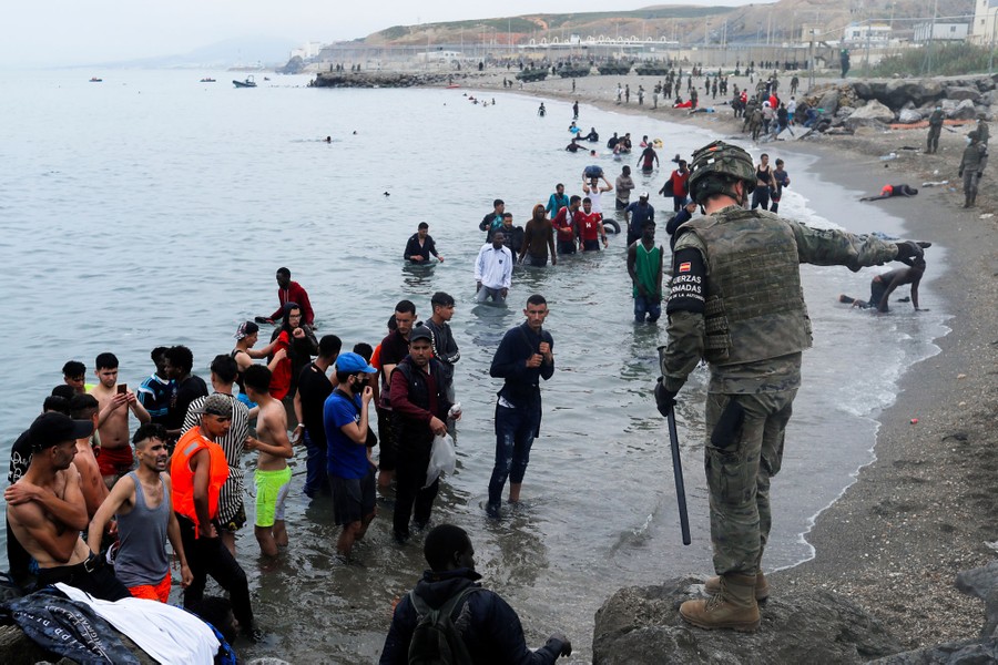 A soldier directs migrants on a beach.