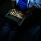 A person typing on a laptop in the dark