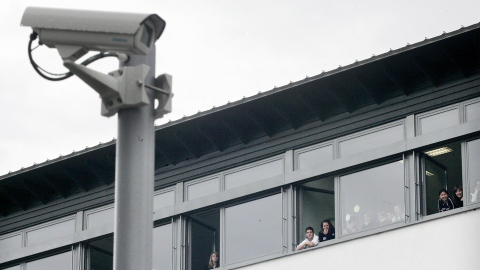A mounted security camera outside a school with students looking out the window