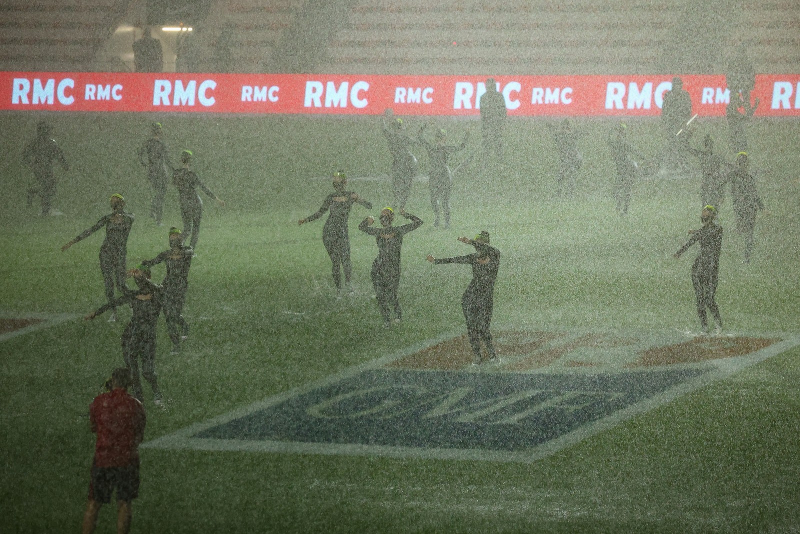 A group of dancers performs on a rugby field during heavy rainfall.
