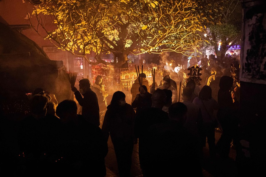 People carry incense sticks while walking around a temple at night.