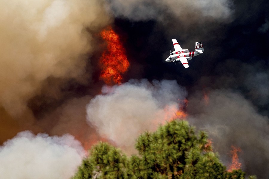 A twin-propeller aircraft flies above a burning forest.