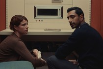 Jessie Buckley and Riz Ahmed sitting together in a retro room