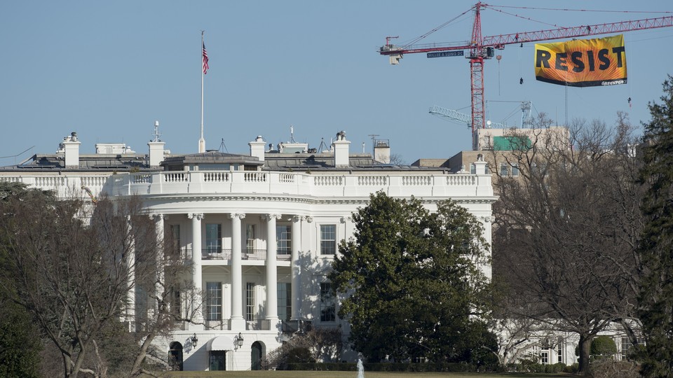 A construction crane with a sign reading RESIST stands behind the White House.