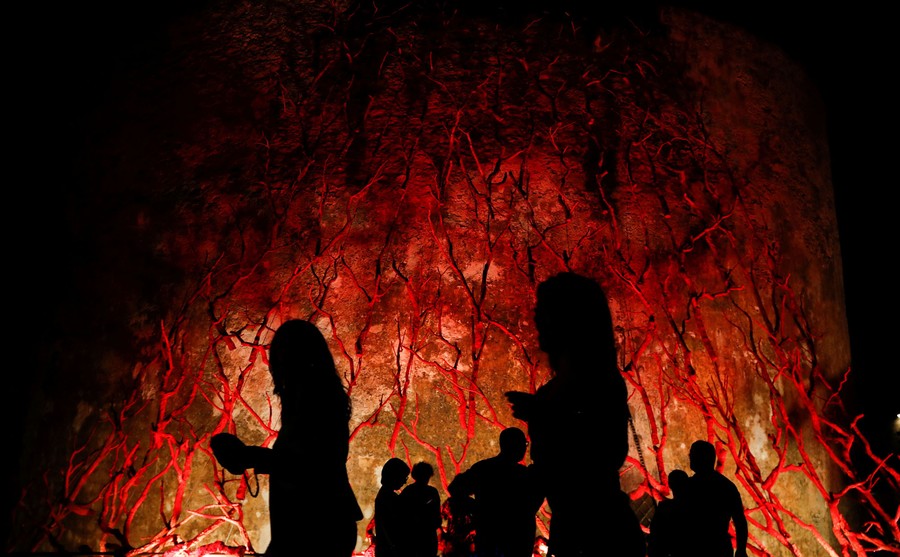 People walk in front of an art exhibit resembling a tree made of coral.