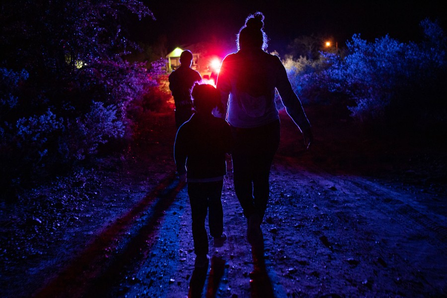 ImageSeveral people and at least one child walk toward red and blue lights among bushes at night.