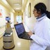 A human caregiver uses a laptop to operate a robot caregiver in the hallway of a nursing residence.