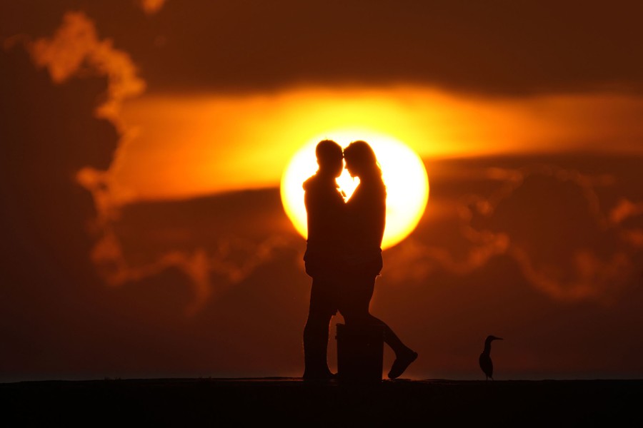 Two people stand close together, silhouetted by the rising sun.