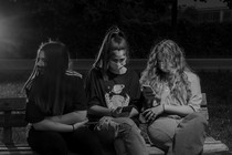 Three teenagers wearing masks look at their phones in a park