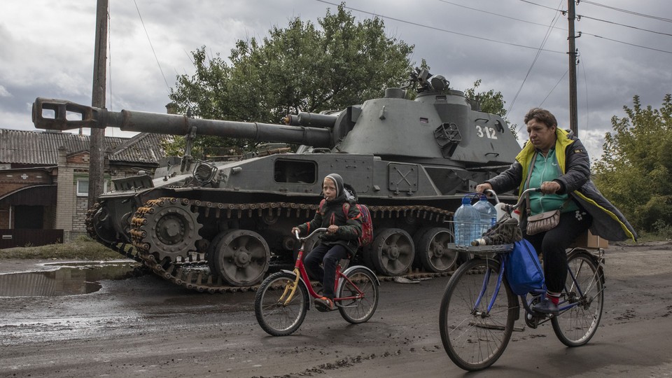 Balakliia residents riding bikes in front of a tank