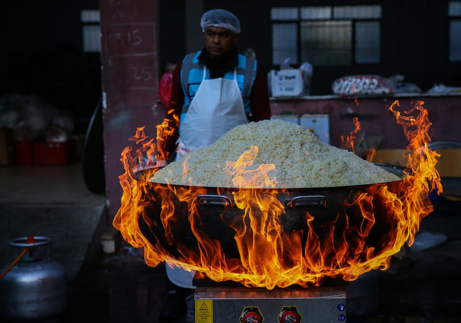 A huge cauldron of rice is cooked over flames.