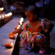 A child kneels down to touch one of many small oil lamps laid out on temple steps.