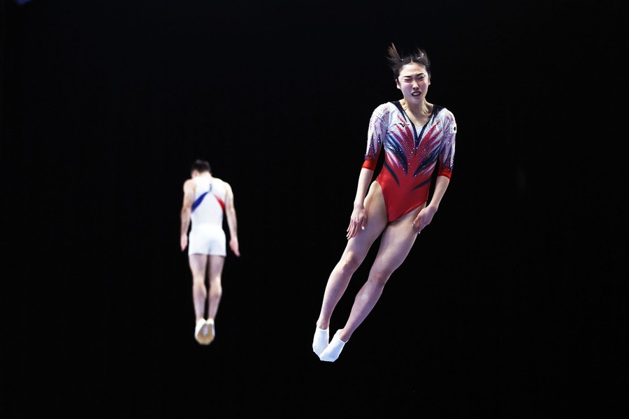 Two athletes perform in a trampoline competition, seen in mid-air.