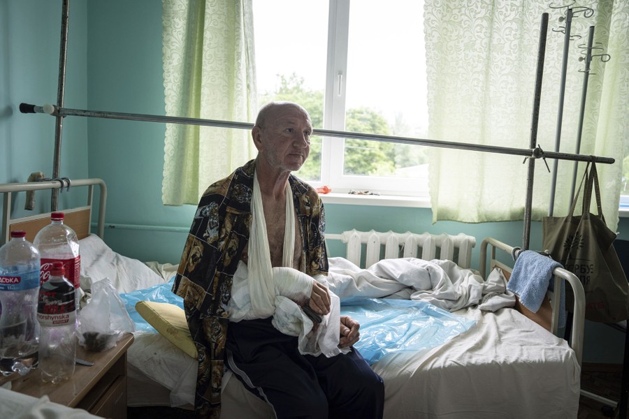 A man sits on the edge of a hospital bed with his bandaged arm in a sling.