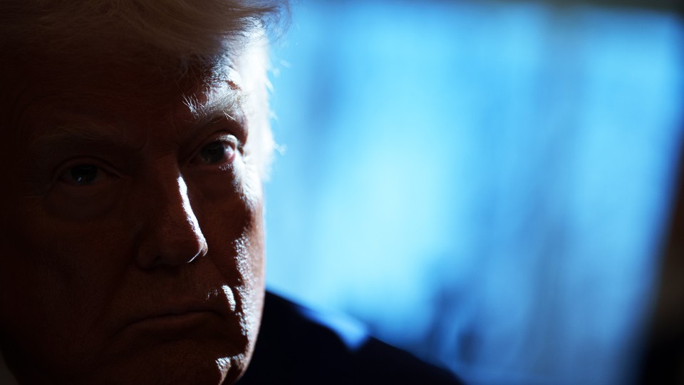 Trump's face, dimly lit and in front of a faded blue screen