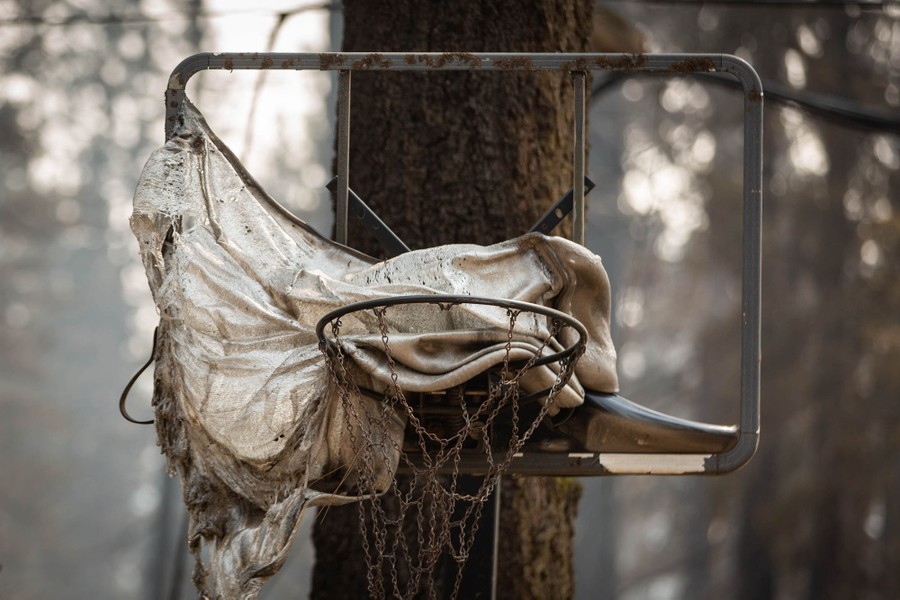 The plastic backboard of a basketball hoop hangs in a melted tangle after a wildfire passed through.