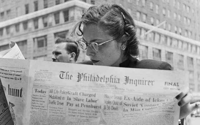 A black and white photograph of a woman reading the Philadelphia Inquirer