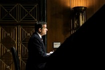 John Ratcliffe sits at a table in a low-lit, wood-paneled room.