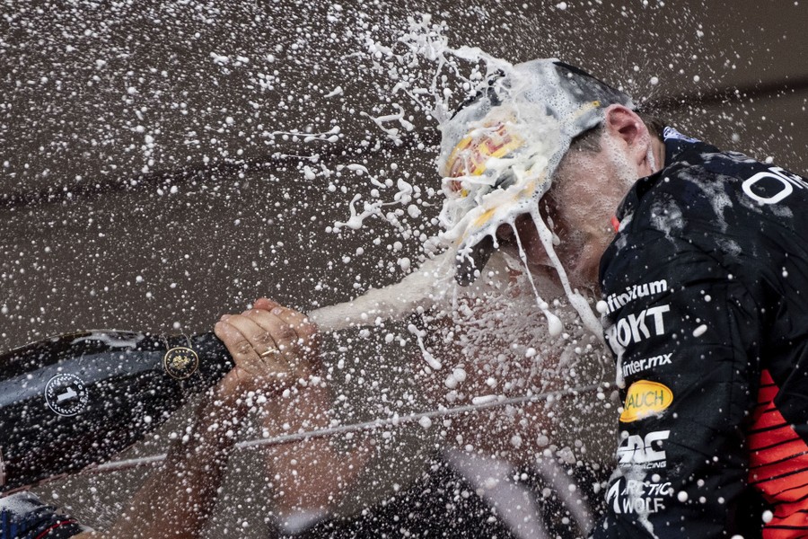 A race-car driver is doused with foamy champagne in celebration.
