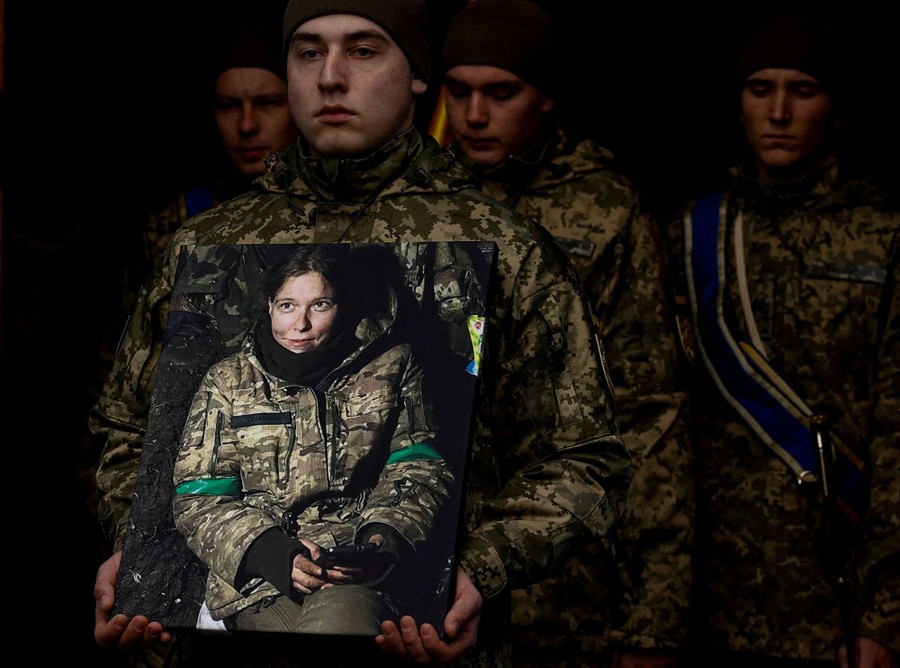 Several soldiers stand together at a funeral; one holds a photograph of another soldier.