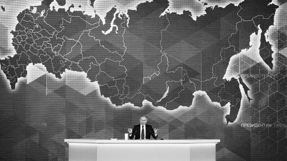Vladimir Putin sits behind a desk and in front of a map.