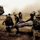 Soldiers on a barren field lift a body on a stretcher, covered in an American flag, into a helicopter.