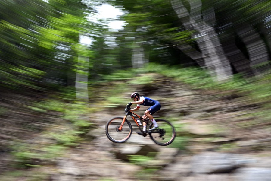 A motion-blurred photo of a racer riding a mountain bike through a forest
