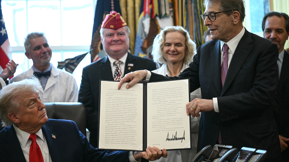 Trump holds up a signed bill in the Oval Office surrounded by smiling onlookers