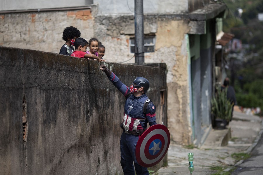 A man dressed as Captain America fist-bumps children standing at a wall above him.