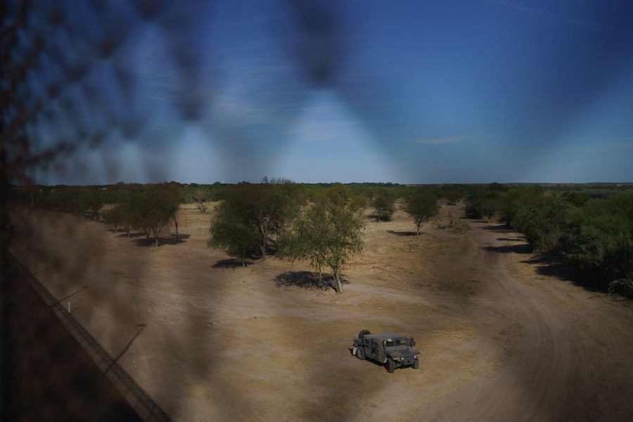 A Humvee sits parked in an empty lot near a bridge.