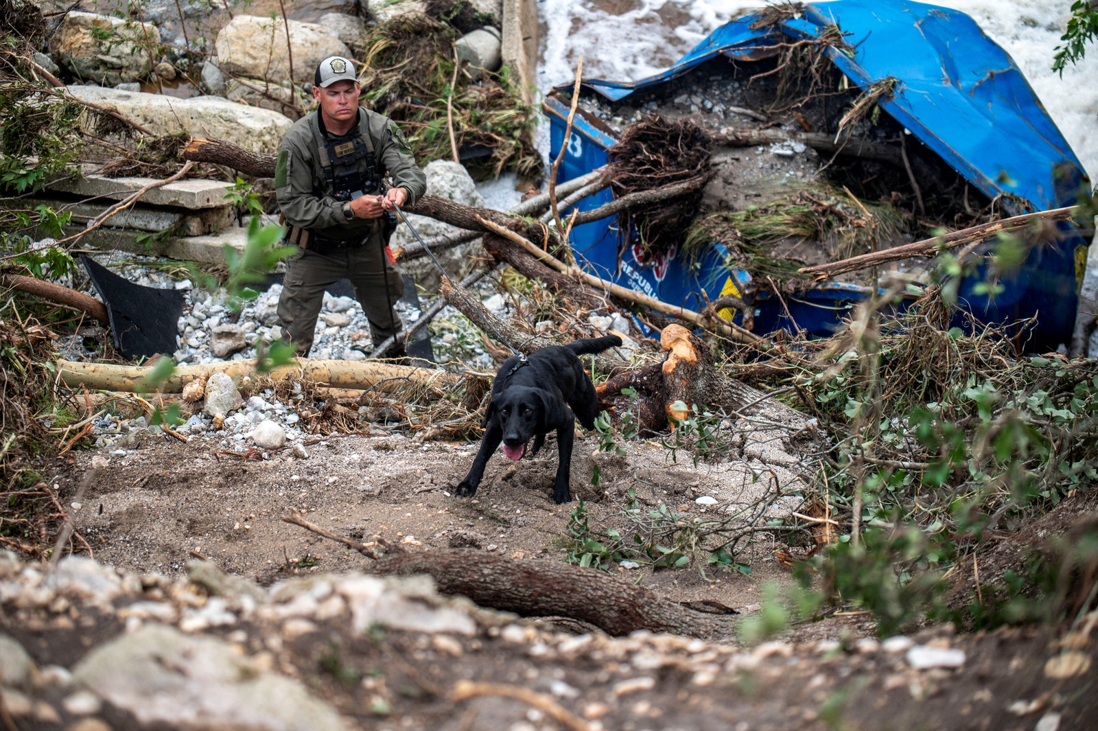 A search dog scrambles over flood debris, pulling at its handler.