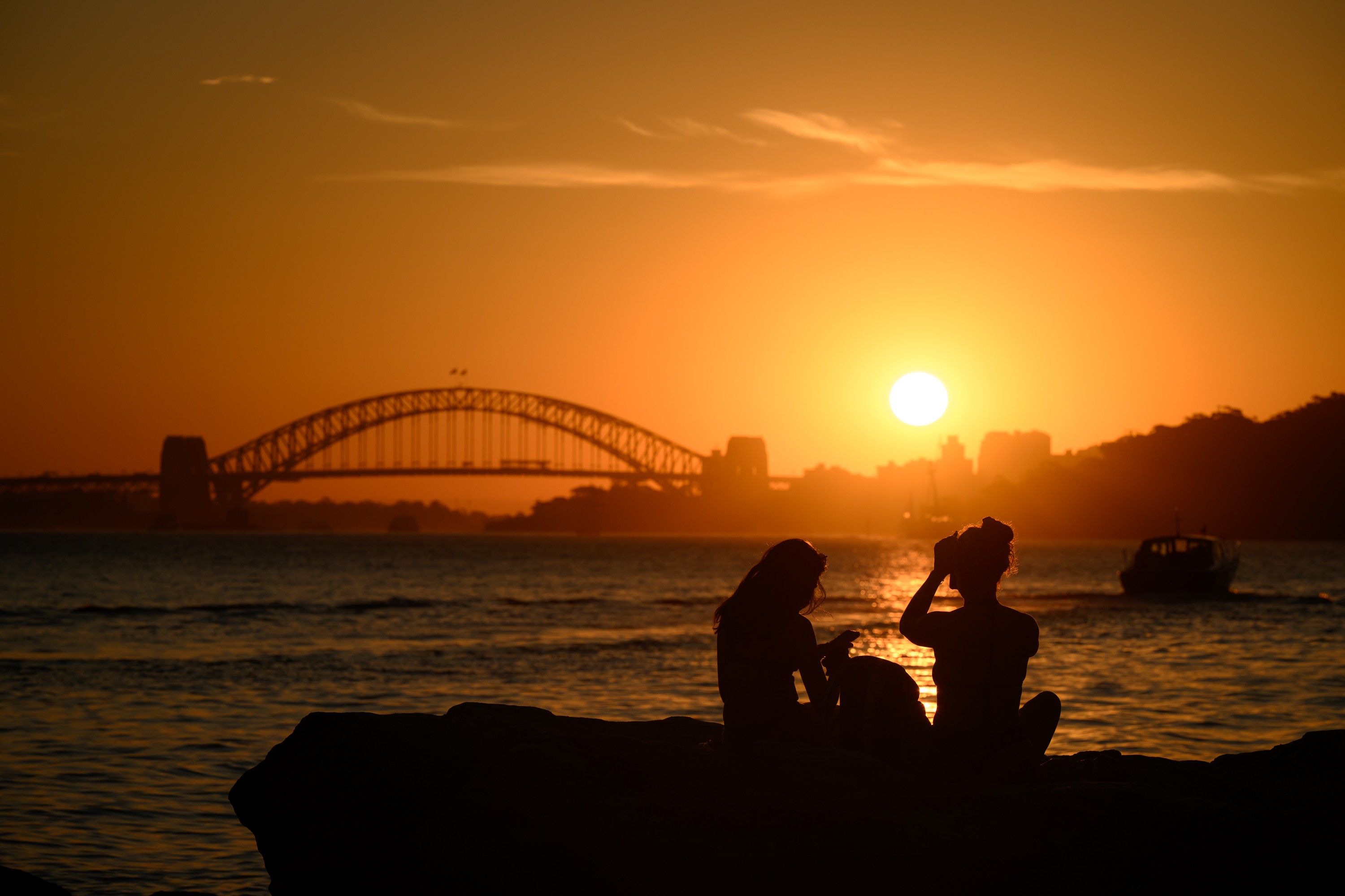 Two people sit out, enjoying the sunset at a beach in Sydney, Australia.