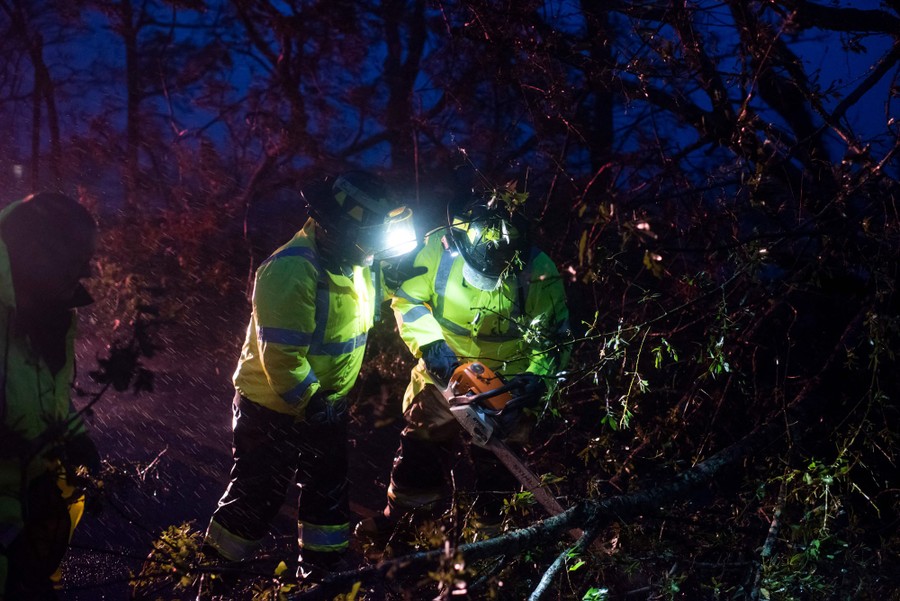 Firefighters cut through fallen trees at night.