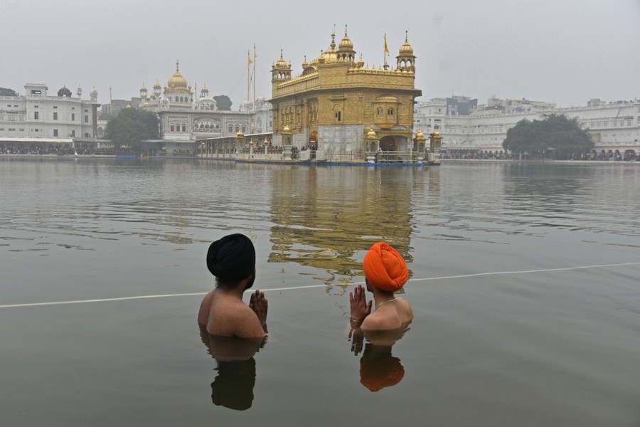 Two men stand in shoulder-deep water, praying, near a temple.