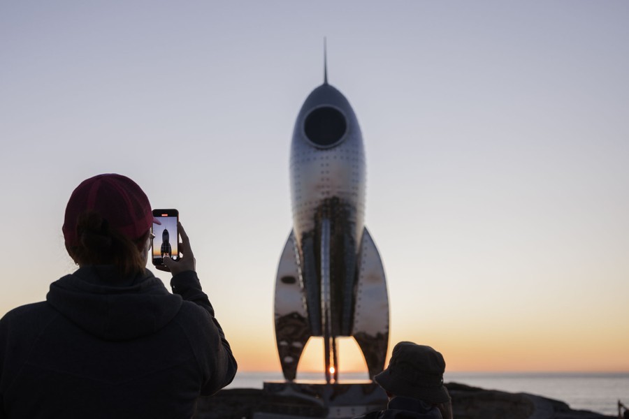 A person takes a photograph of a sculpture shaped like a fanciful rocket ship.