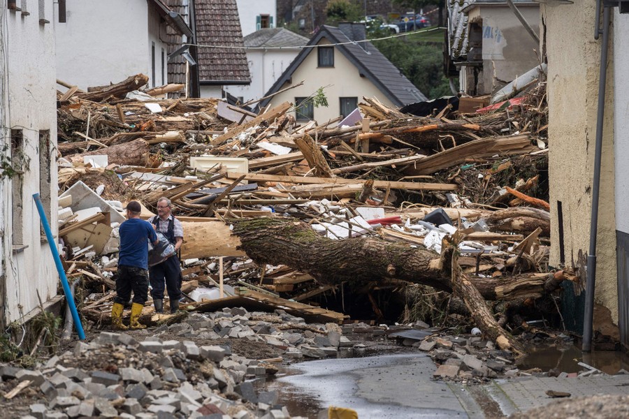 Two men work in a street, surrounded by giant piles of debris.