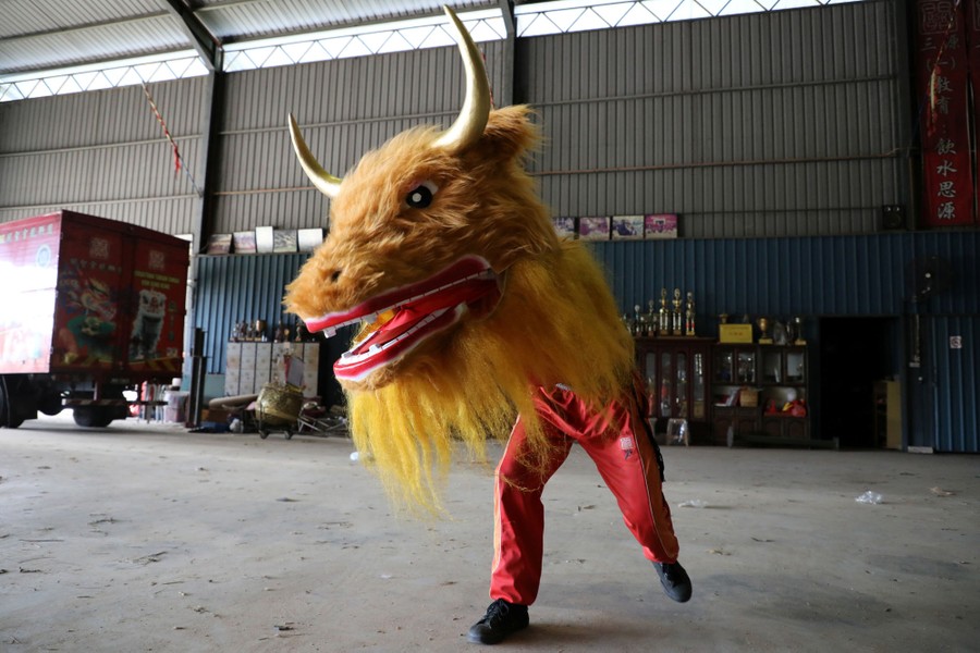 A dancer wears a large furry dragon head inside a warehouse.
