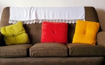 A brown couch with three throw pillows—one green, one red, one yellow—and a white blanket on the back