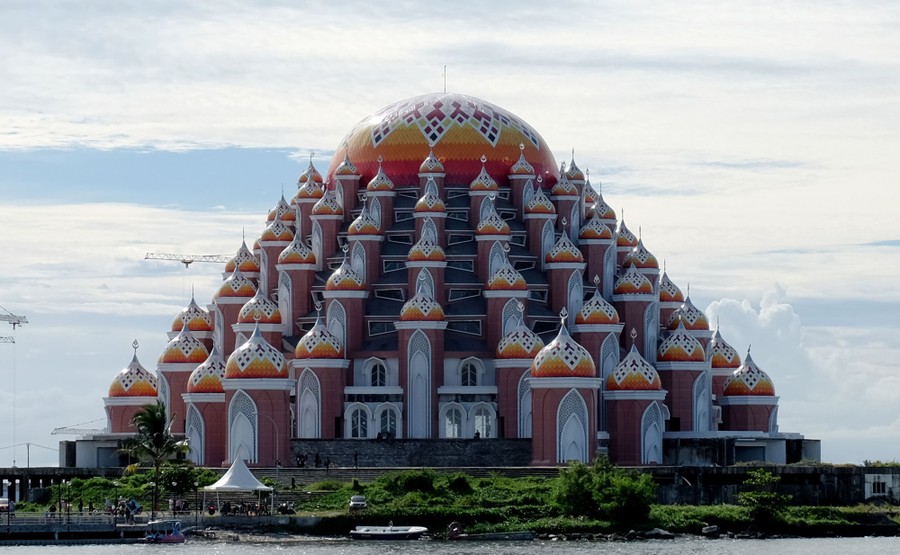 A tall building with many domes sits along a shoreline.