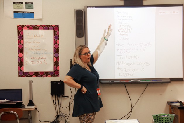 A teacher gestures to a Smart Board.