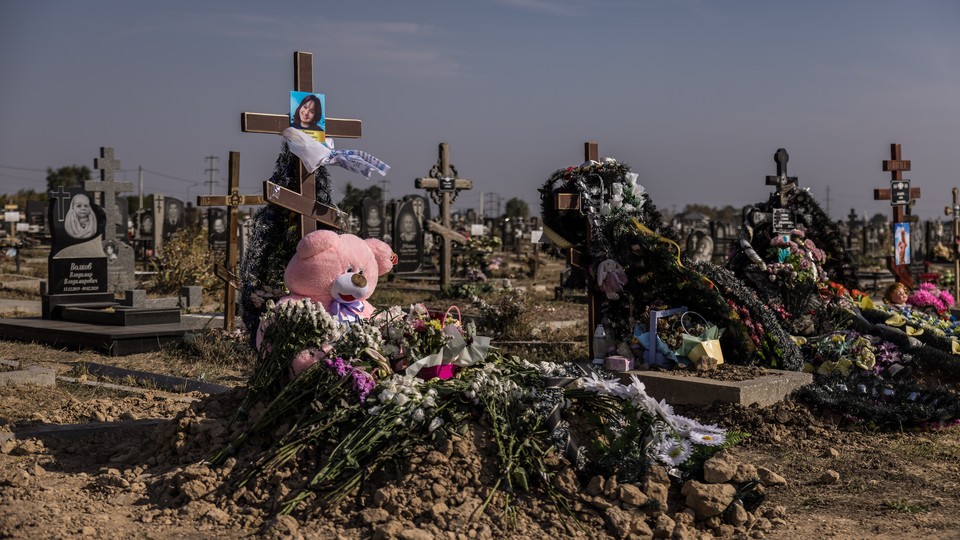 Rows of crosses for the Ukrainian victims of a Russian bomb attack. One cross has an image of a girl and a pink teddy bear underneath.