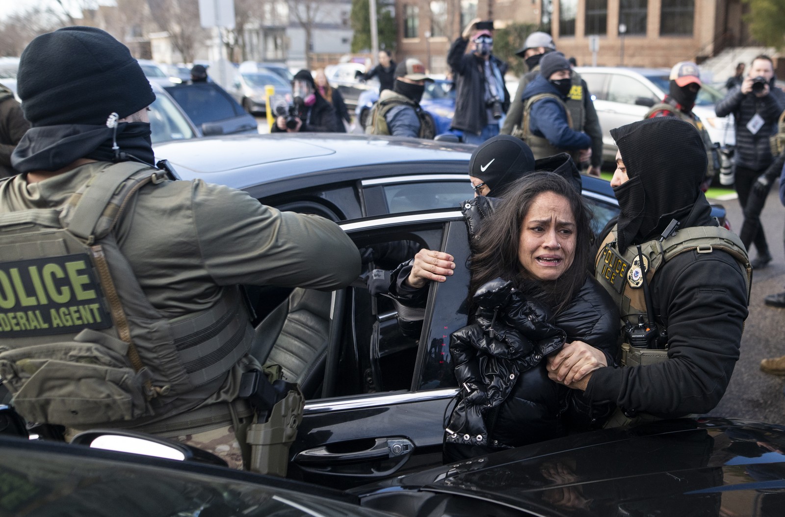 A woman reacts as she is dragged from a car by several masked federal agents in a residential street.