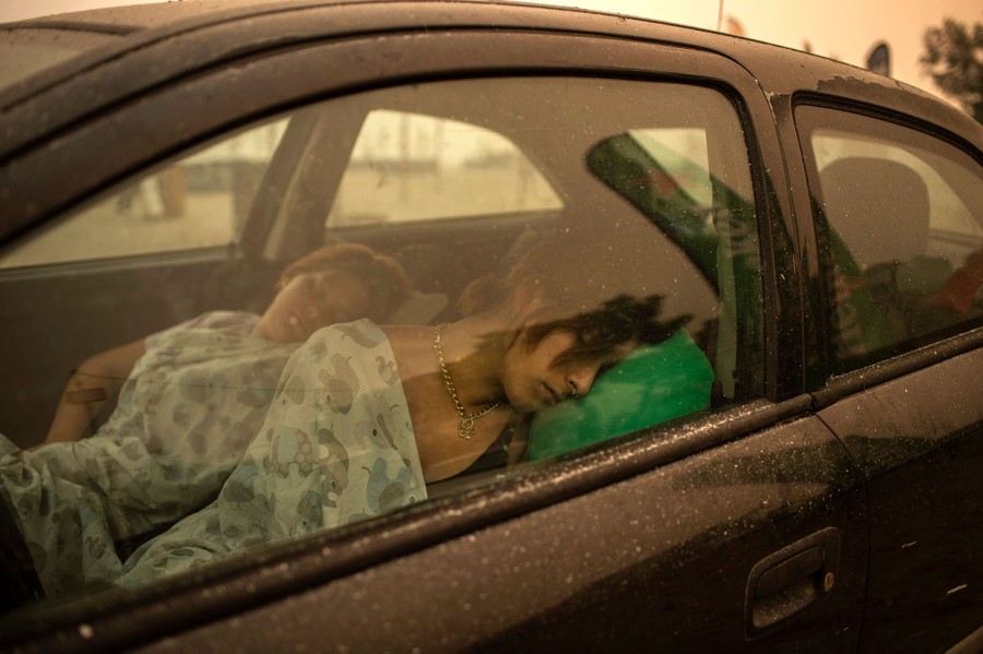 People sleep in a car on the beach under smoky skies.
