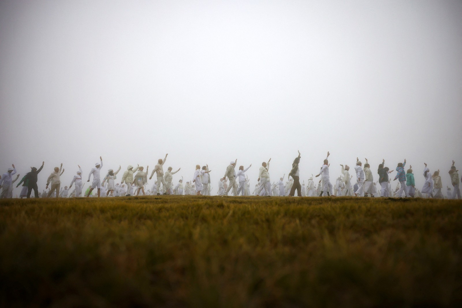 A group of people all wearing all-white clothing perform a sort of dance in a foggy mountain field.